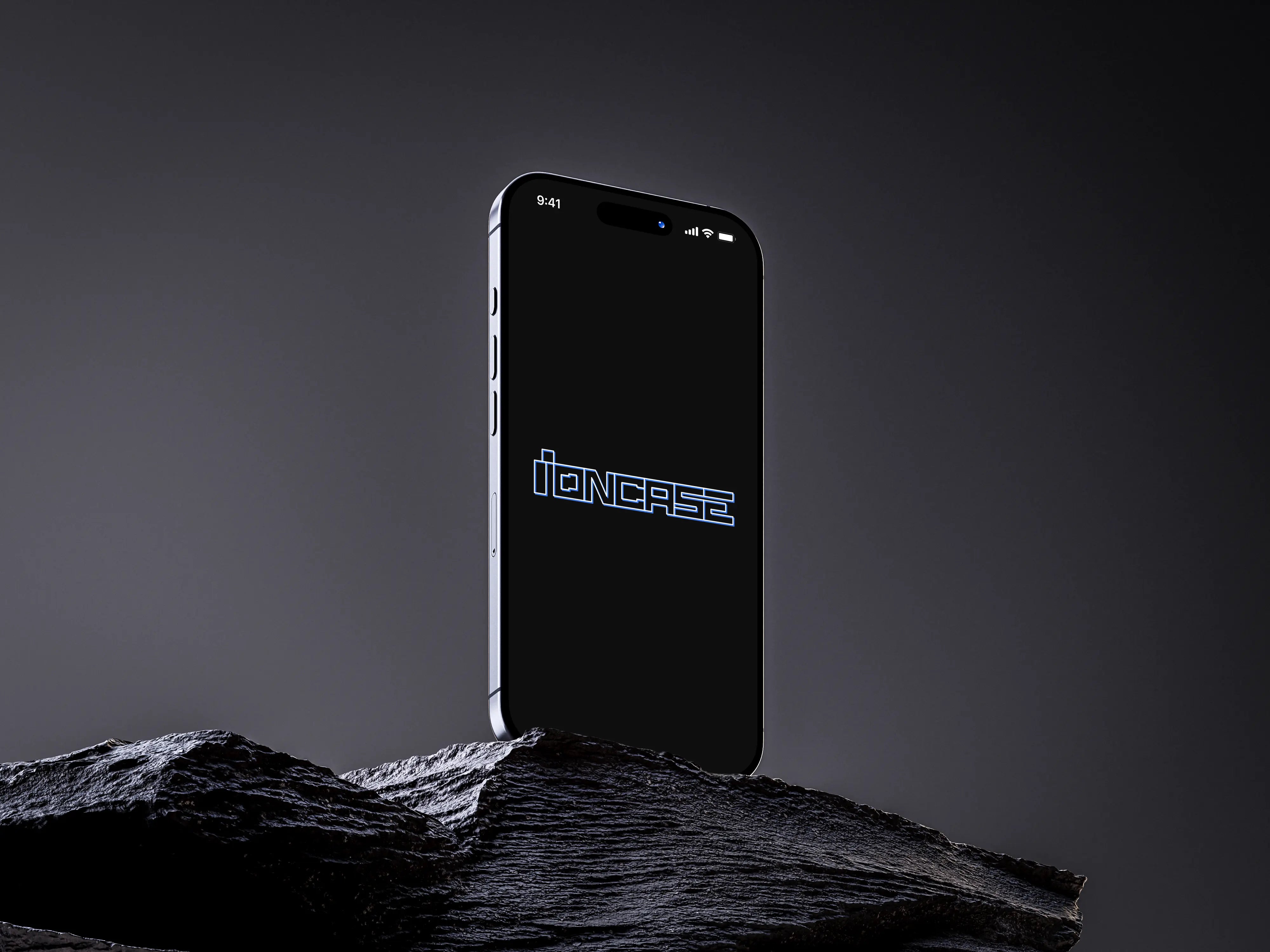 Photo studio d'un iPhone 16 Pro Max avec écran allumé affichant le logo IONCASE posé sur un bloc de graphite